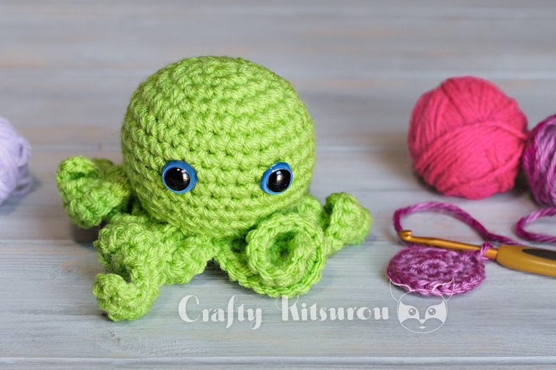 Green crocheted octopus surrounded by yarn and crochet hook.