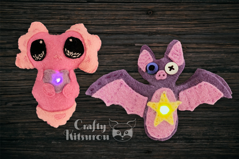 Sewn felt figures with LEDs. One is a  pink axolotl holding a heart, and the other is a purple bat with a yellow star on its belly.